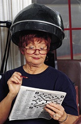 Lady sitting under hair dryer, solving a crossword